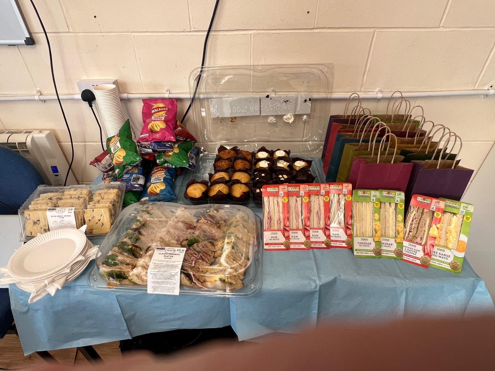 A table laid out with sandwiches, cakes, drinks and welcome gift bags for Open Day guests